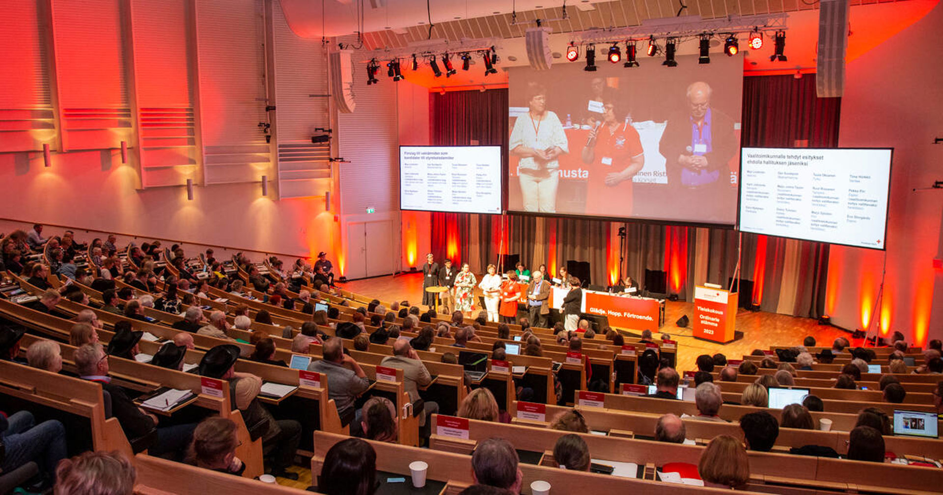 Ihmisiä punaiseksi valaistussa auditoriossa.
