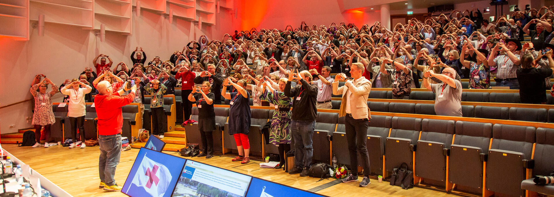Yleisö näyttää käsillään sydäntä seminaaritilassa.