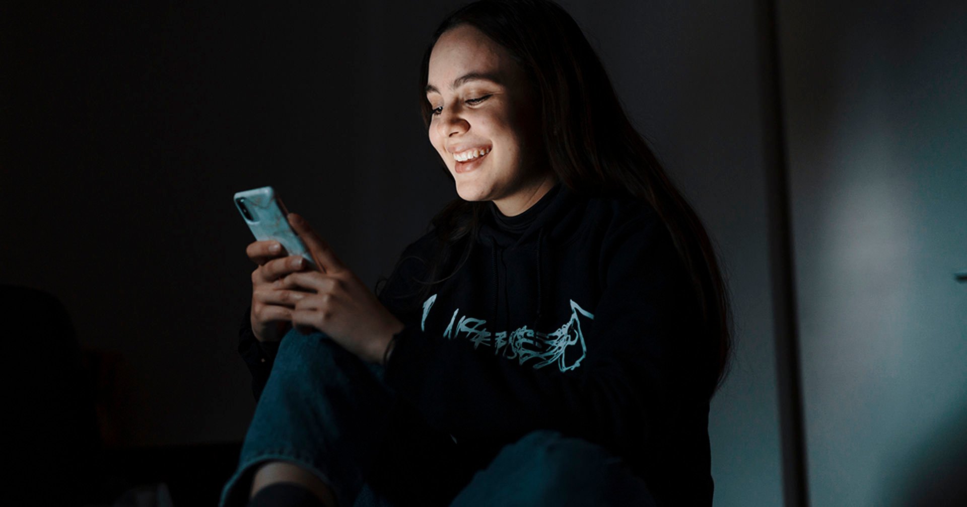 Henkilö katsoo puhelinta ja hymyilee.