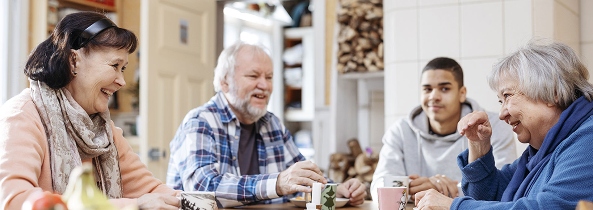 Neljä henkilöä juttelemassa ja juomassa kahvia pöydän ääressä.