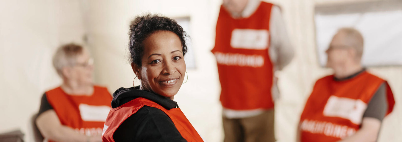 Ryhmäkuva ihmisistä ringissä, etualalla hymyilevä nainen katsoo kameraan