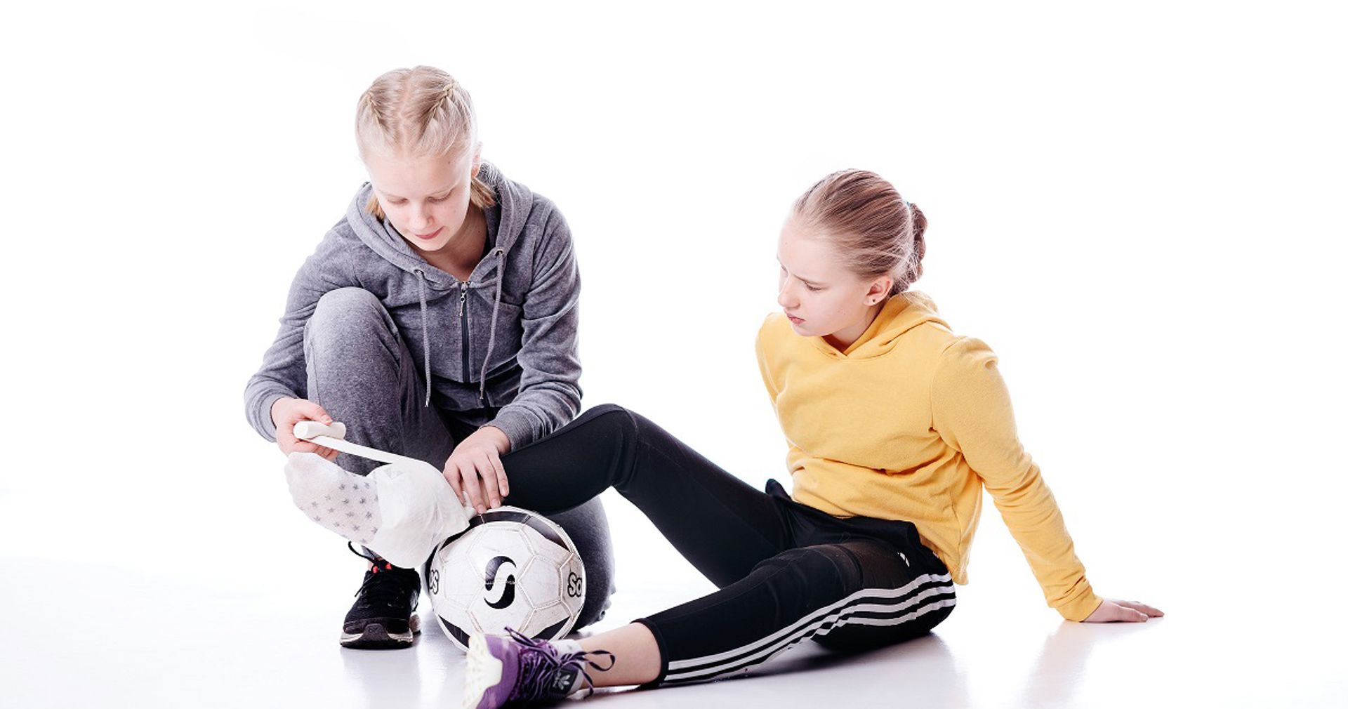 Nuori auttaa toista nuorta, joka on loukannut jalkansa jalkapallossa.