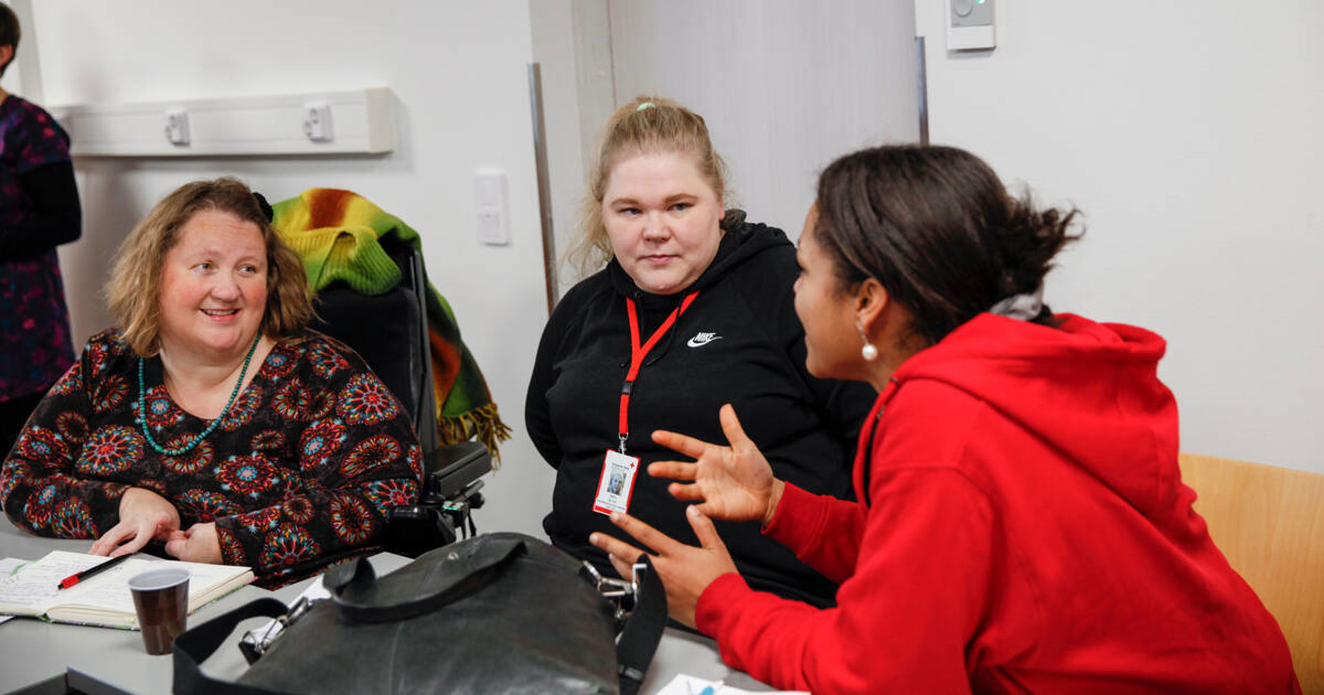 Vapaaehtoiset juttelevat pöydän ääressä. Yksi heistä on pyörätuolissa.