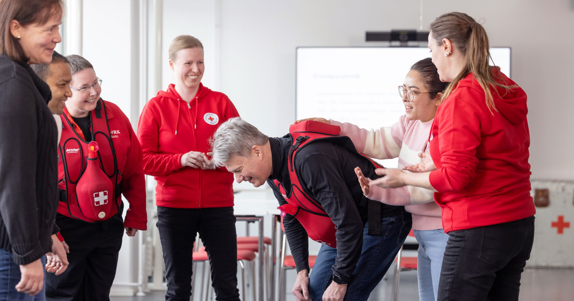 Vapaaehtoiset hymyilevät ringissä. Yksi on kumartuneena keskellä.