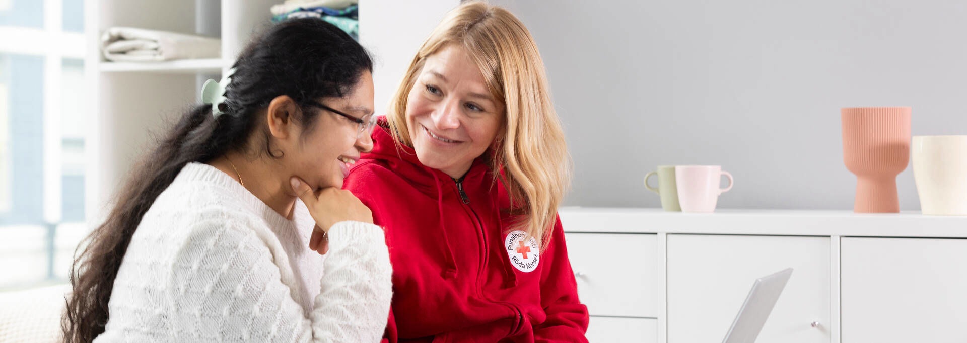 Vapaaehtoinen opastaa osaston uutta työntekijää, jolla on tietokone sylissään.