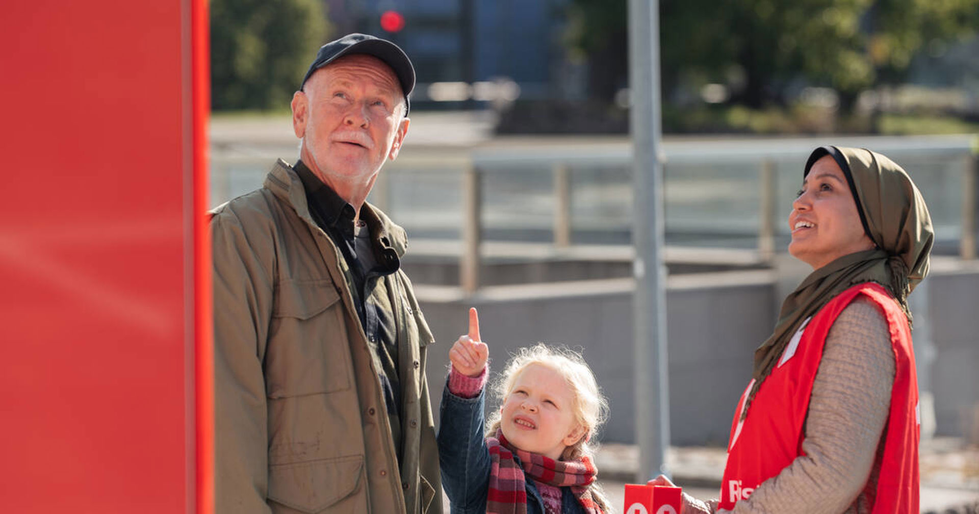 Kolme henkilöä. Yhdellä henkilöllä on yllään Punaisen Ristin vapaaehtoisliivi ja kädessä keräyslipas.