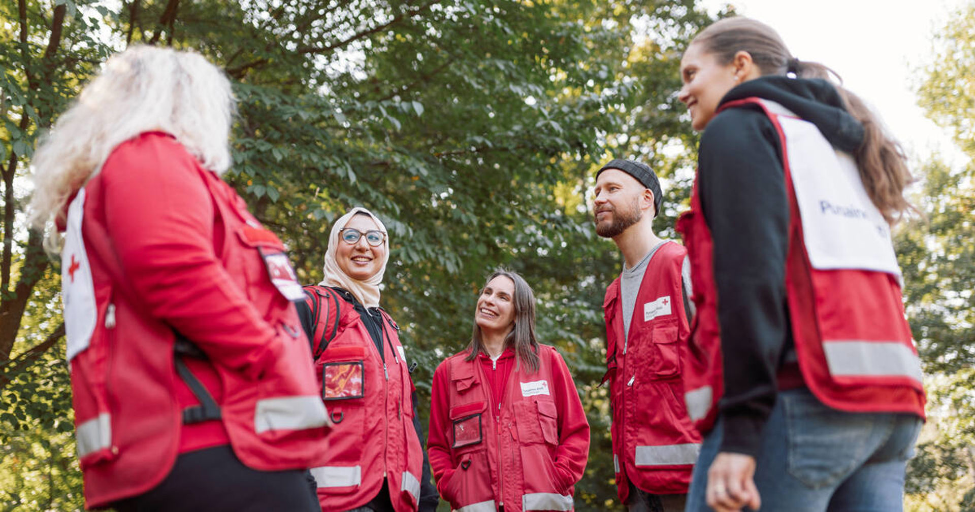 Ryhmä vapaaehtoisia keskustelemassa. Kaikilla on yllään Punaisen Ristin vapaaehtoisliivit.