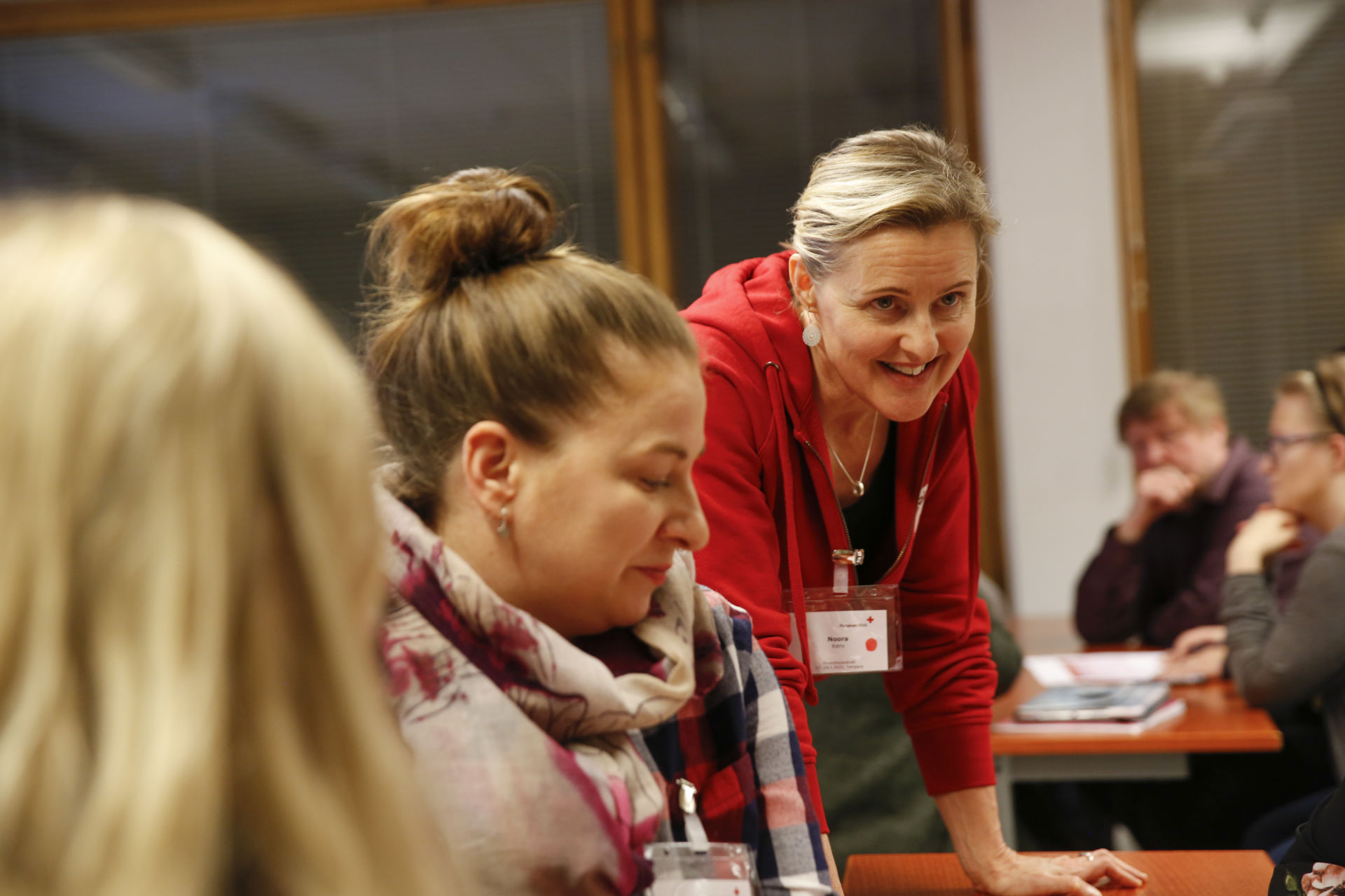 Suomen Punaisen Ristin kouluttaja nojaa pöytään ja hymyilee koulutettaville.