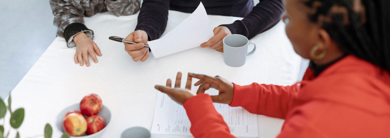 Suomen Punaisen Ristin vapaaehtoinen keskustelee pöydän ääressä aikuisen ja lapsen kanssa.