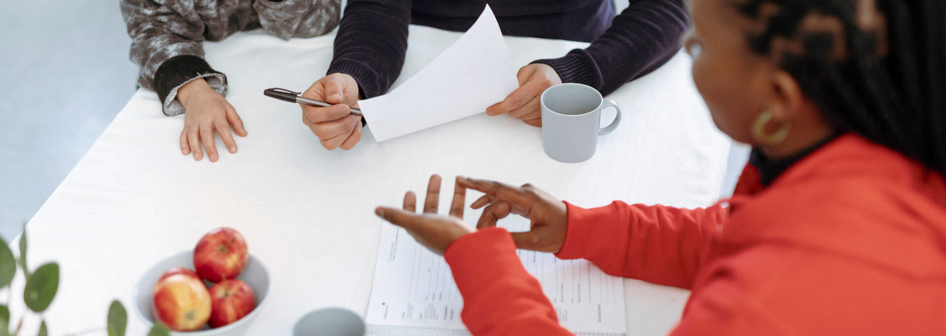 Suomen Punaisen Ristin vapaaehtoinen keskustelee pöydän ääressä aikuisen ja lapsen kanssa.