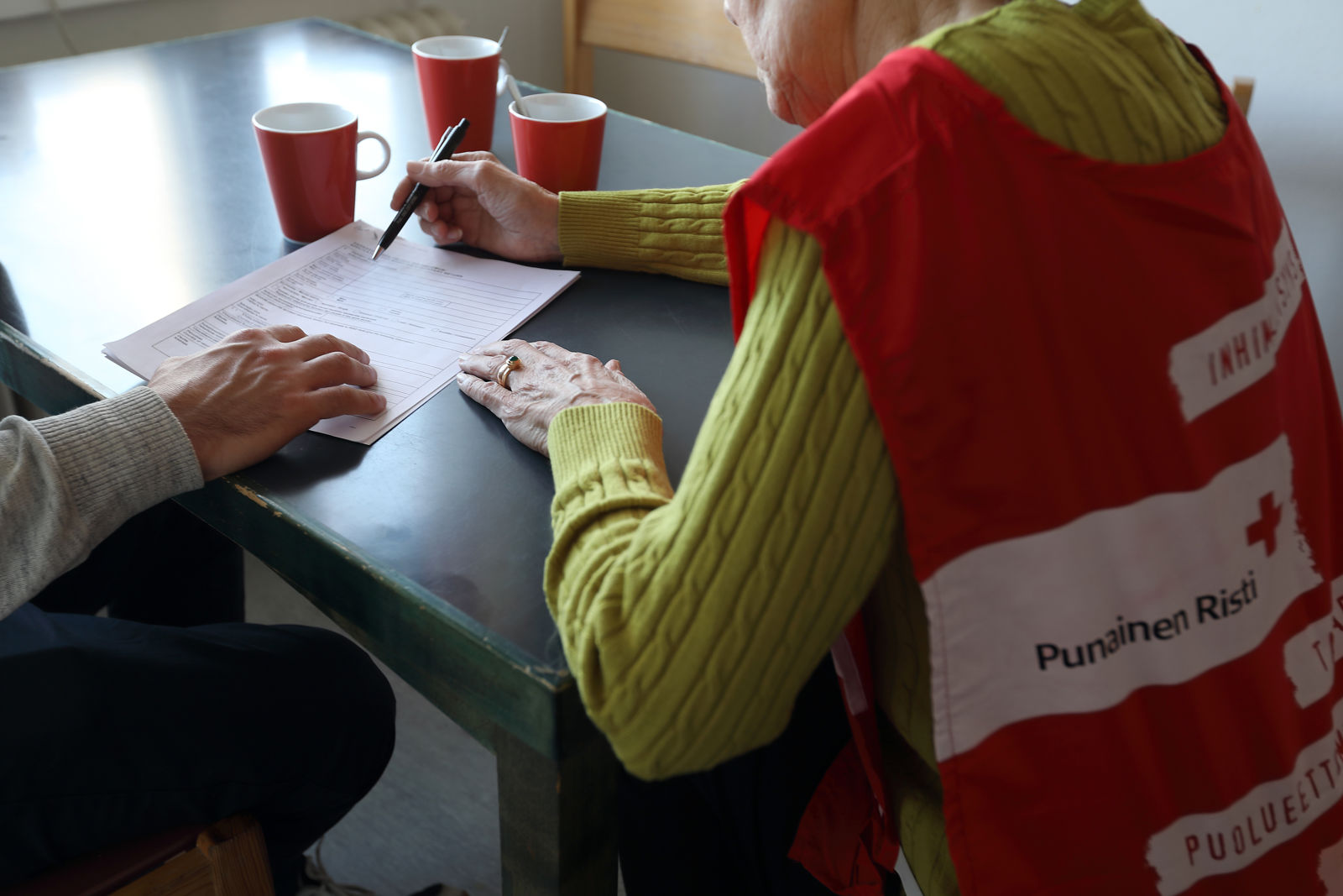 Suomen Punaisen Ristin vapaaehtoinen auttaa henkilöä täyttämään lomaketta.