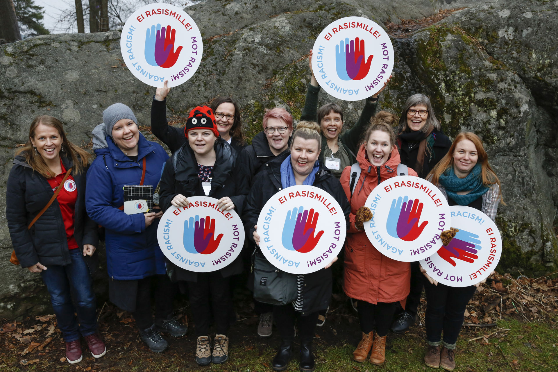 Rymäkuva maahanmuuttotyön kouluttajista ulkona. Heillä on käsissään Rasisminvastaisen kampanjan logoja.