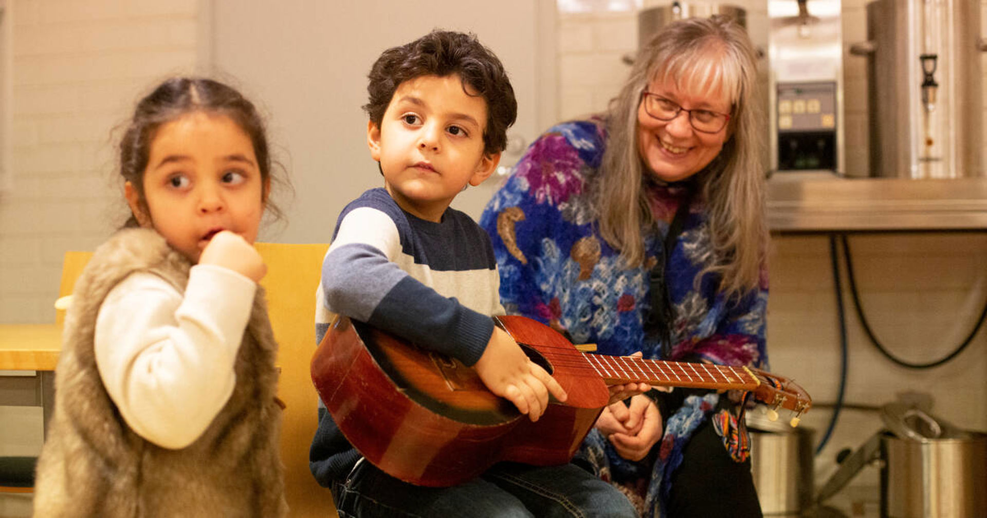 Kaksi lasta ja aikuinen katsovat kitaraa.