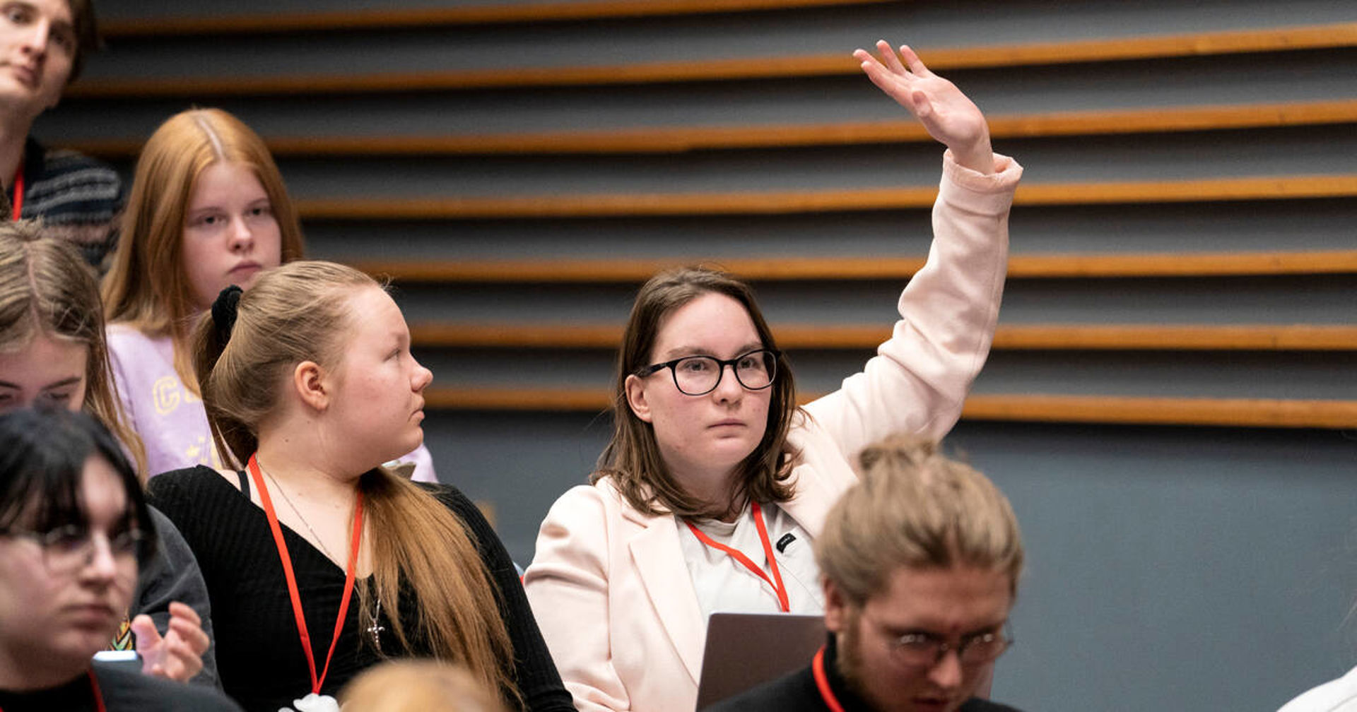 Kuvassa on nuoria kokouksessa. Yksi nuorista viittaa pyytäen puheenvuoroa.