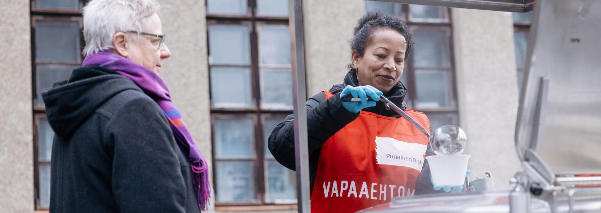 Ruoka-avun vapaaehtoinen annostelee soppaa ruoka-avun hakijalle