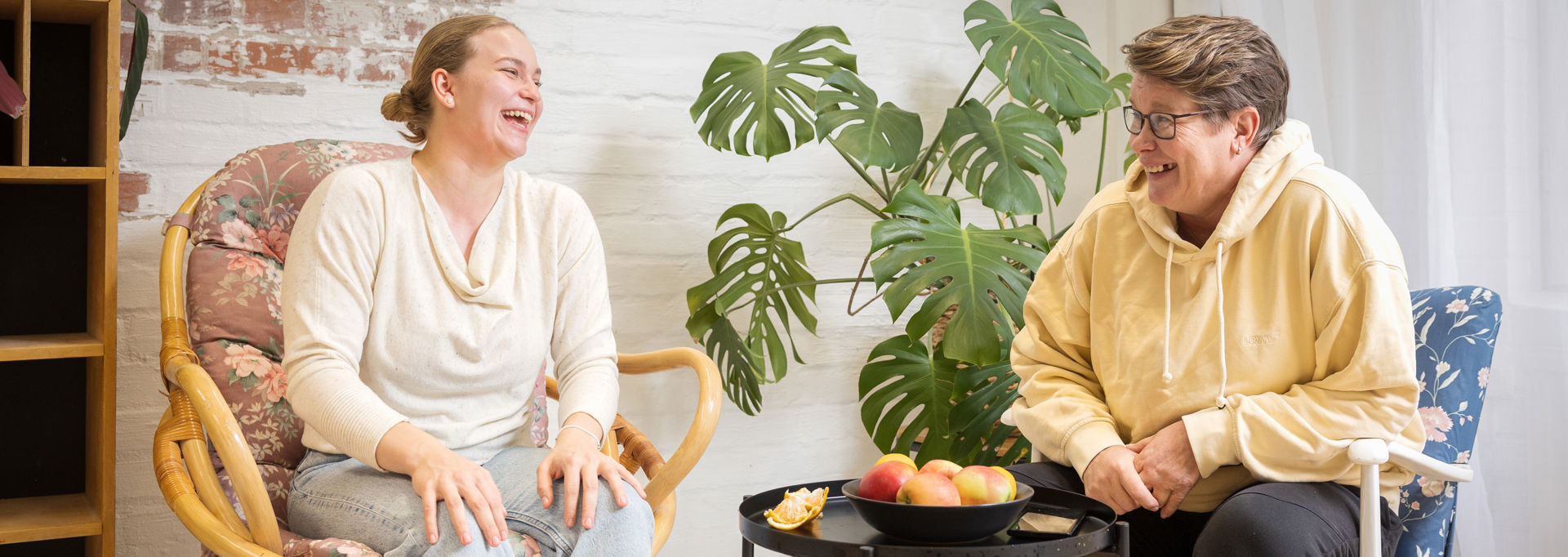 Kaksi henkilöä nauraa sohvapäydän ääressä.