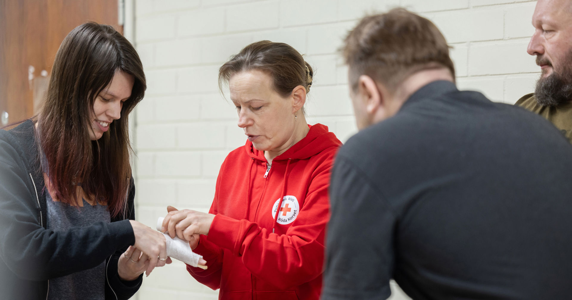 Punaisen Ristin päihdetyön vapaaehtoinen sitoo henkilön käteen sidettä.