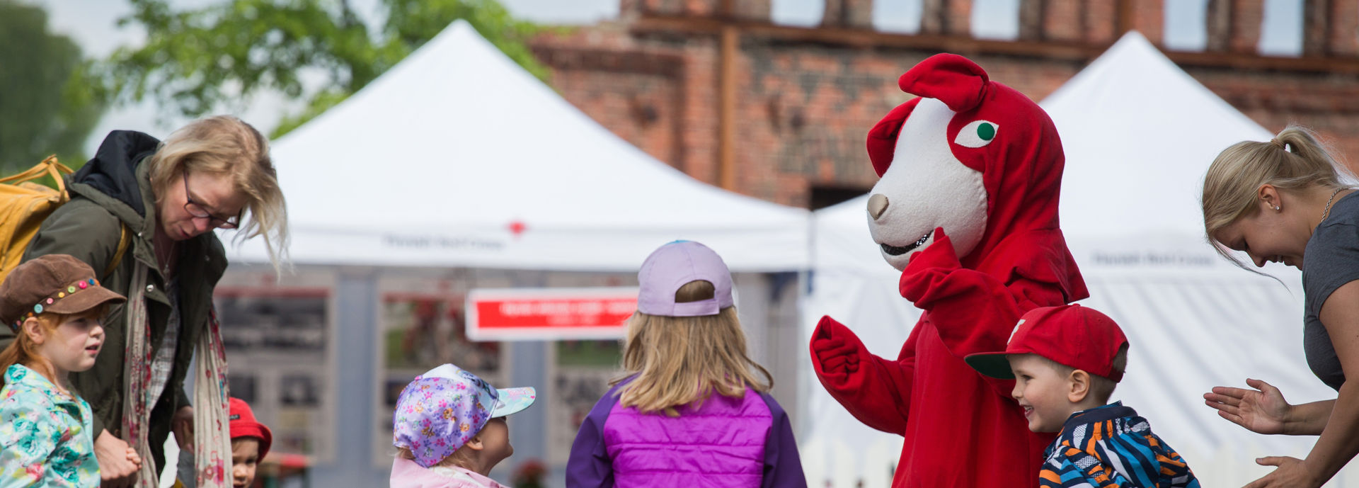 Lapset tanssivat Reddie-koiran kanssa ulkotapahtumassa.