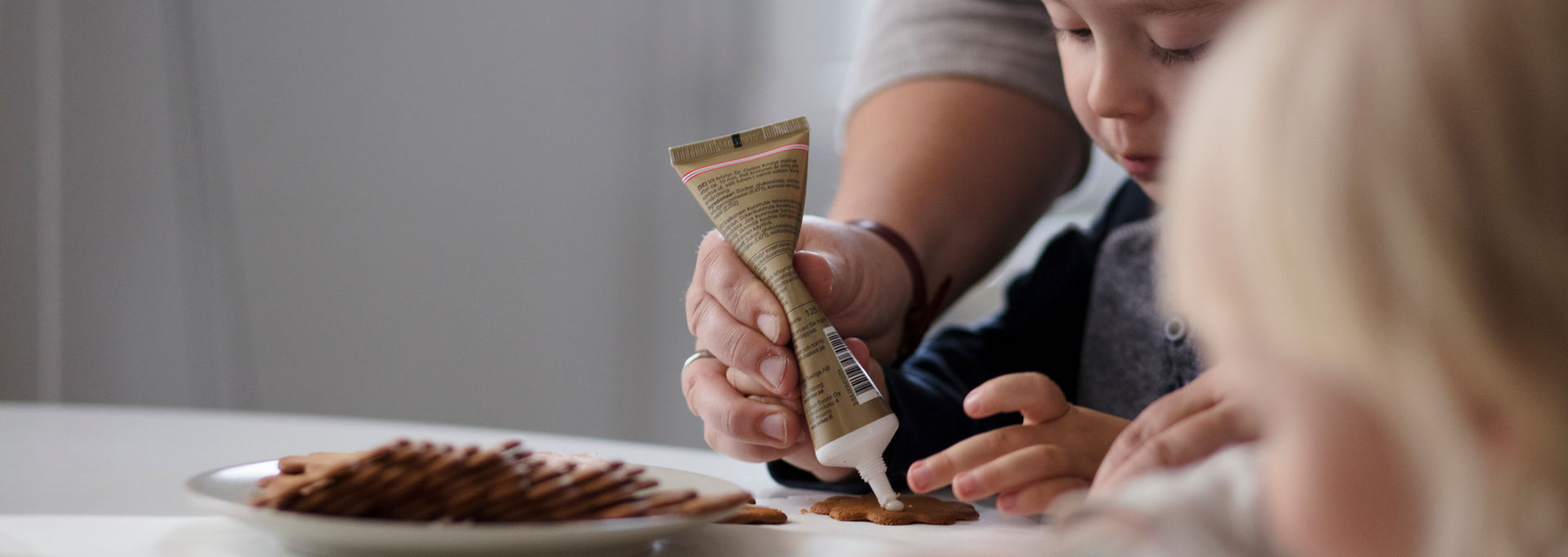 Lapsi koristelee piparkakkuja aikuisen kanssa.