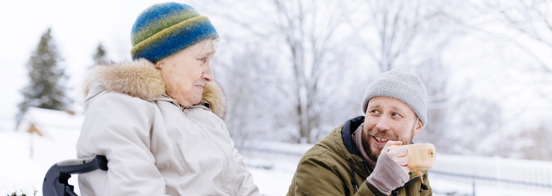 Kaksi henkilöä juttelevat ja juovat kupeista ulkona talvella.