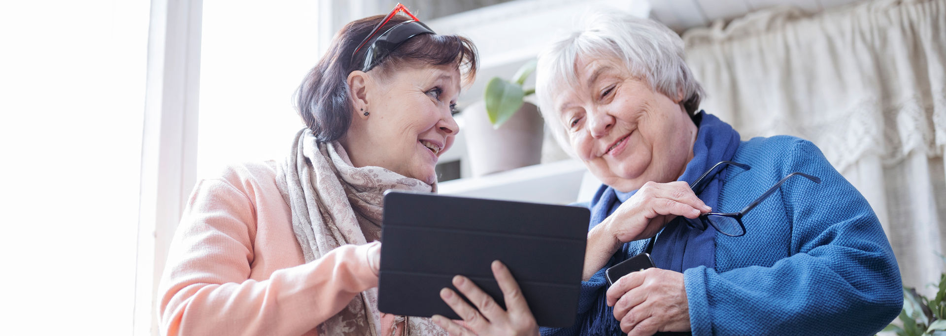 Kaksi henkilöä katsoo tablettia hymyillen.