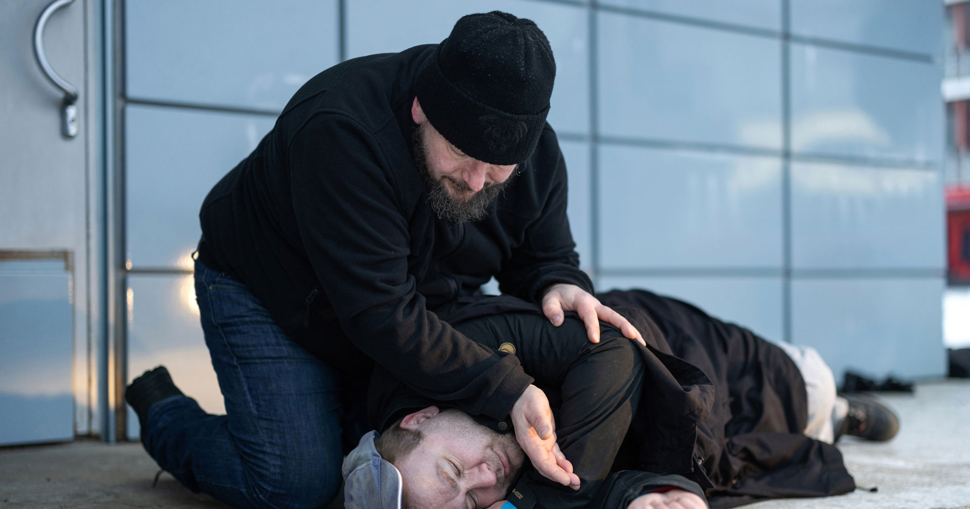 Henkilö makaa maassa ja toinen varmistaa kädellään, hengittääkö tämä.