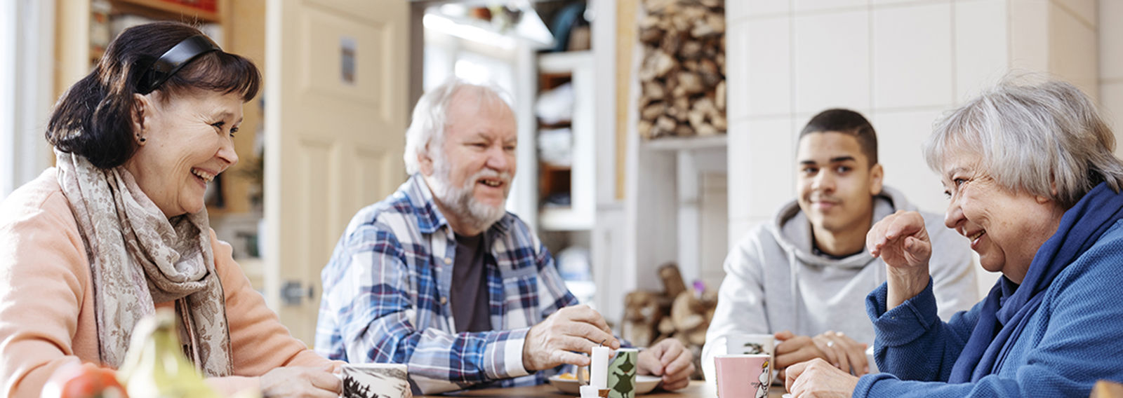 Neljä henkilöä juttelemassa ja juomassa kahvia pöydän ääressä.
