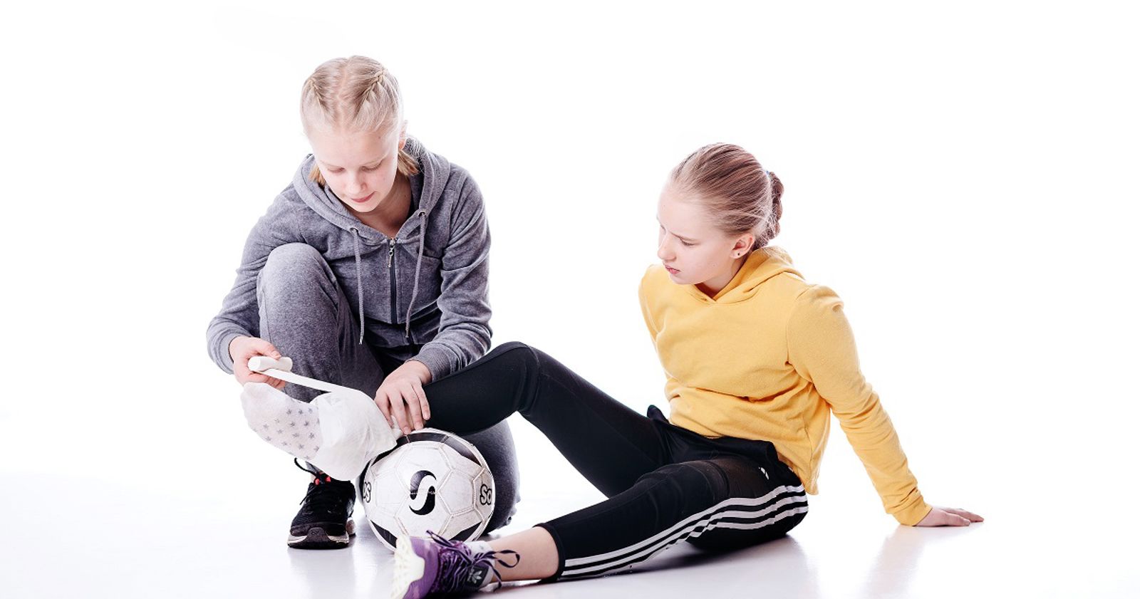 Nuori auttaa toista nuorta, joka on loukannut jalkansa jalkapallossa.