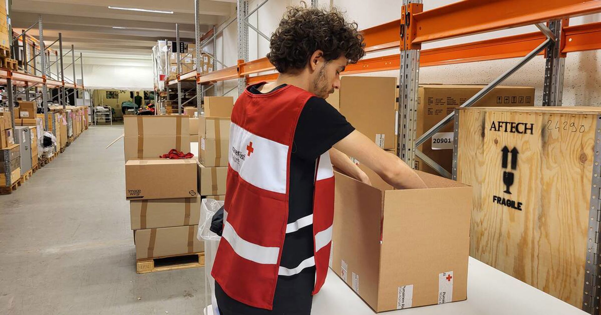 Suomen Punaisen Ristin vapaaehtoinen ottaa jotain laatikosta uusi vapaaehtoisliivi päällään.