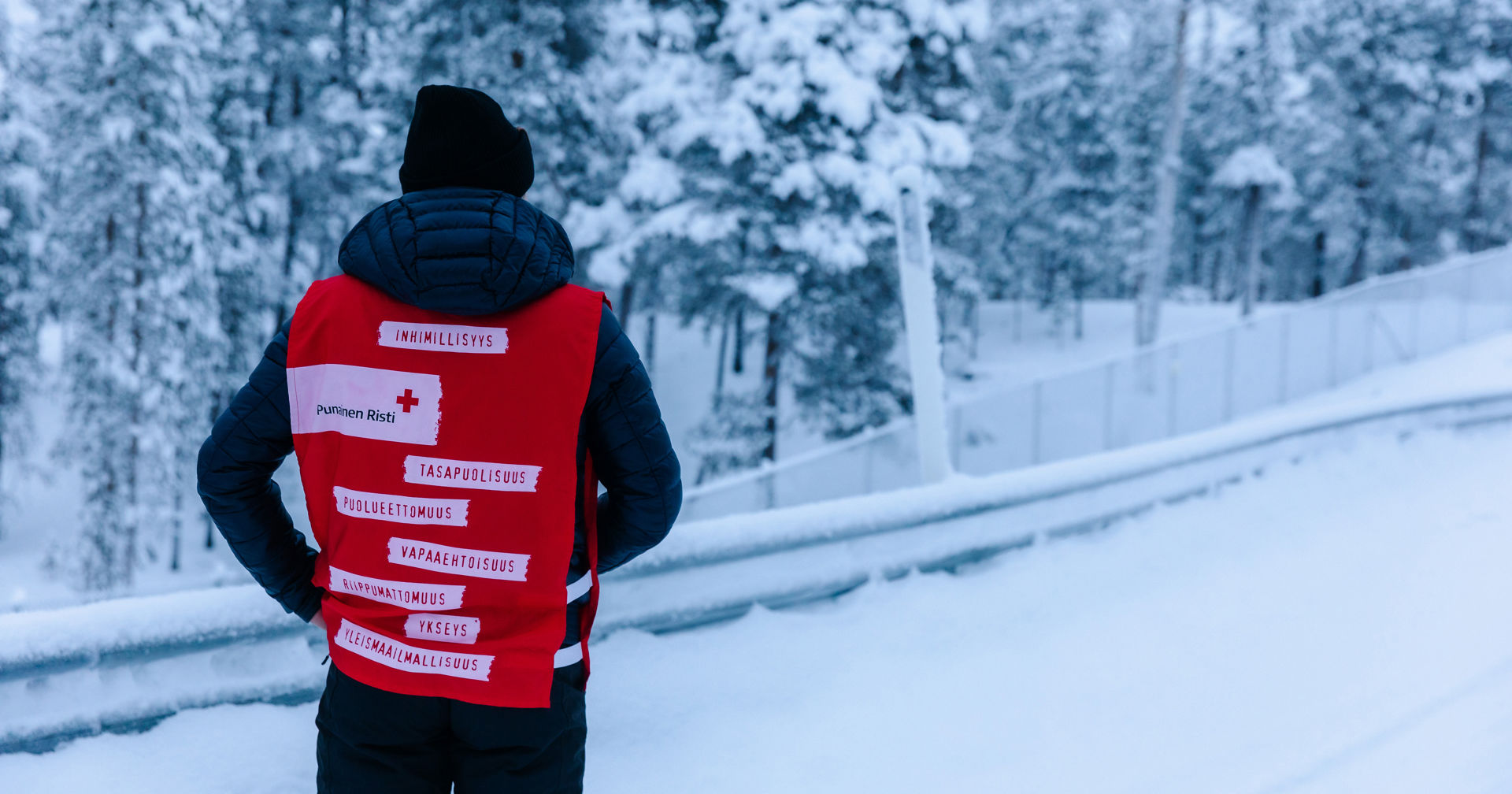Vapaaehtoinen selkä kameraan päin päällään vapaaehtoisliivi, jossa lukee Punaisen Ristin seitsemän periaatetta.