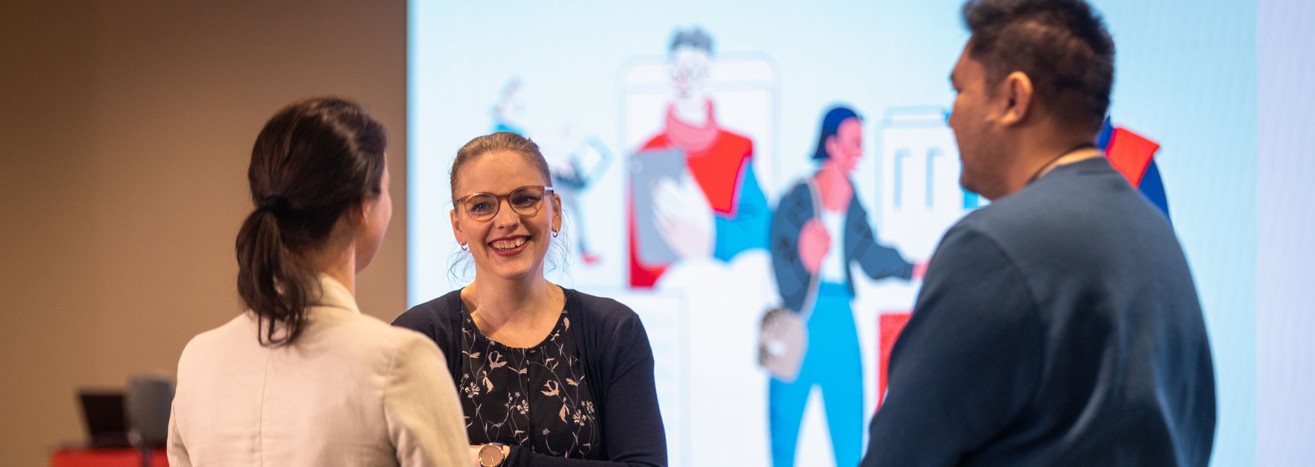 Kolme henkilöä keskustelee tapahtumassa. Taustalla Punaisen Ristin kuvitusta.