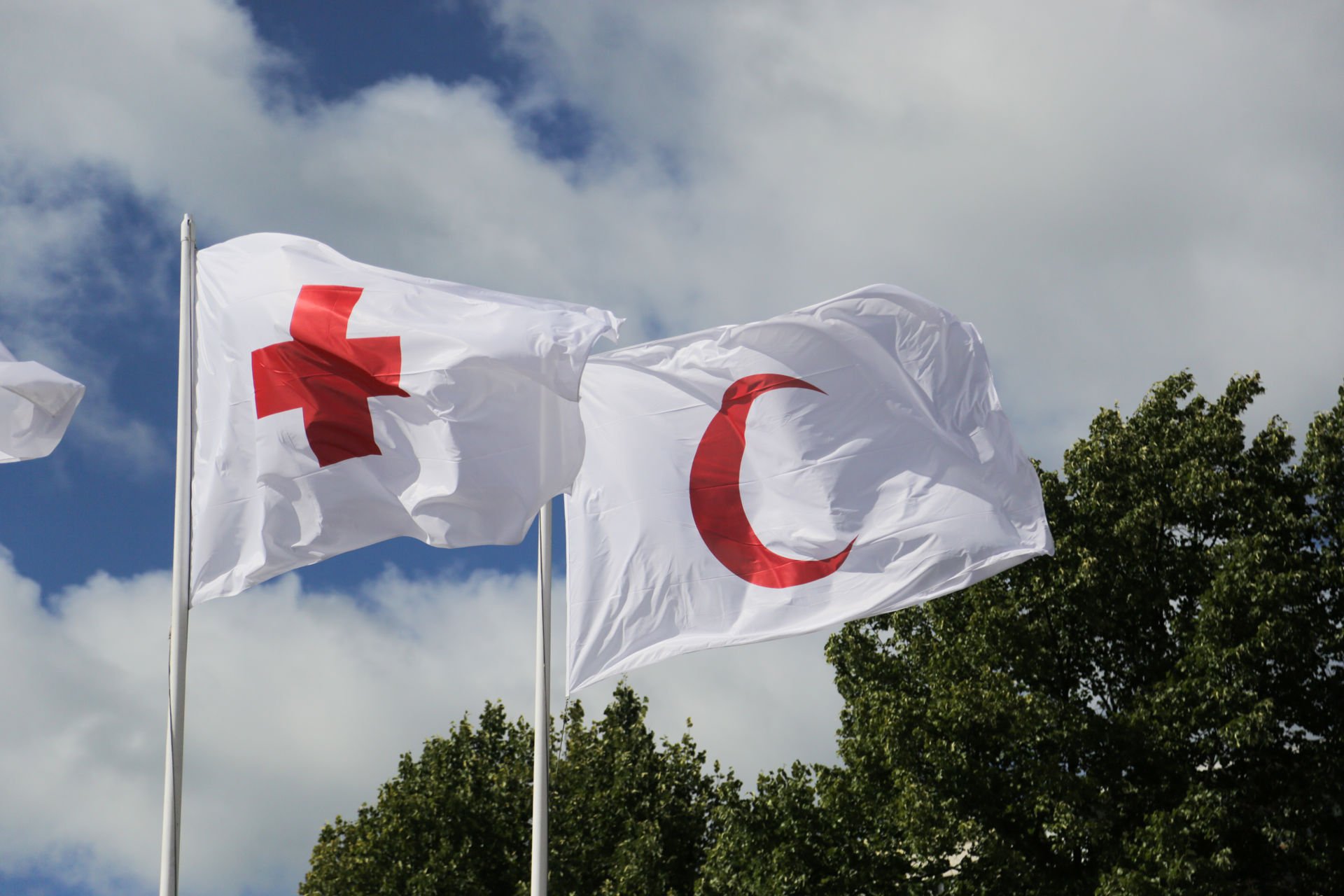 Kaksi lippua lipputangoissa. Toisessa lipussa on Punaisen Ristin ja toisessa Punaisen Puolikuun symboli.