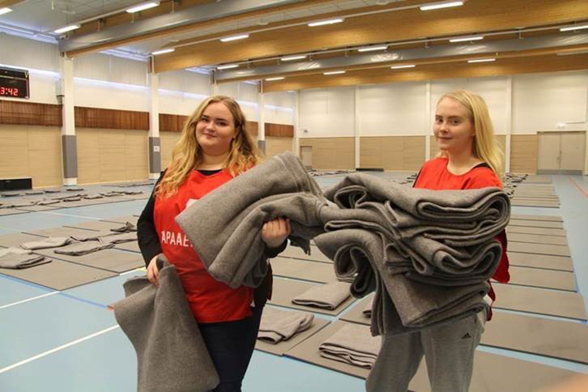 Kaksi Suomen Punaisen Ristin vapaaehtoista pitelee vilttejä liikuntasalissa.