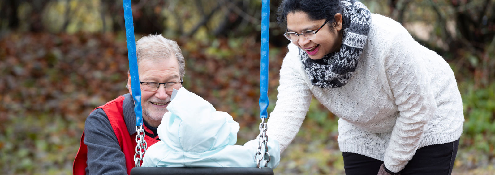 Punaisen Ristin vapaaehtoinen ja henkilö työntävät lasta keinussa.