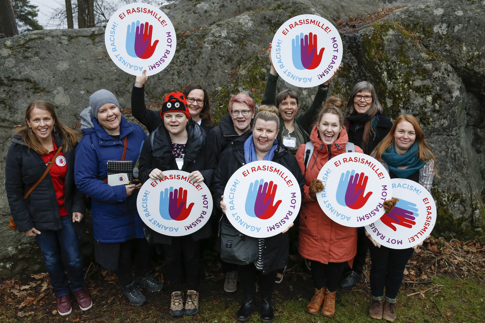 Rymäkuva maahanmuuttotyön kouluttajista ulkona. Heillä on käsissään Rasisminvastaisen kampanjan logoja.