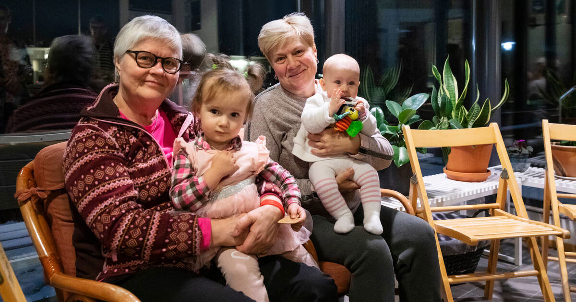 Kaksi aikuista lapset sylissään hymyilee kameraan.