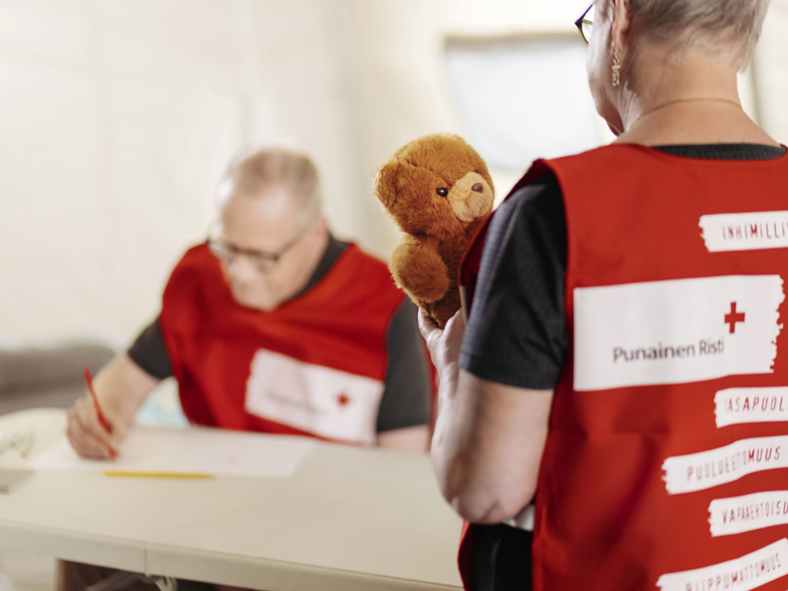 Toinen nallesairaalan vapaaehtoinen kirjoittaa taustalla paperille ja toisella on nalle käsissään.