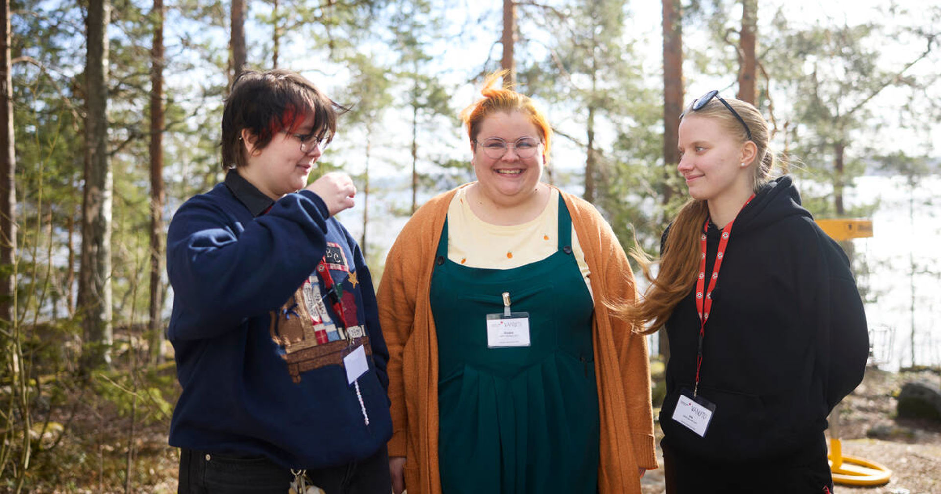Kolme Punaisen Ristin nuorta vapaaehtoista seisovat rinnakkain ulkona ja juttelevat iloisesti. Keskimmäinen henkilö kuvassa katsoo kohti kameraa.