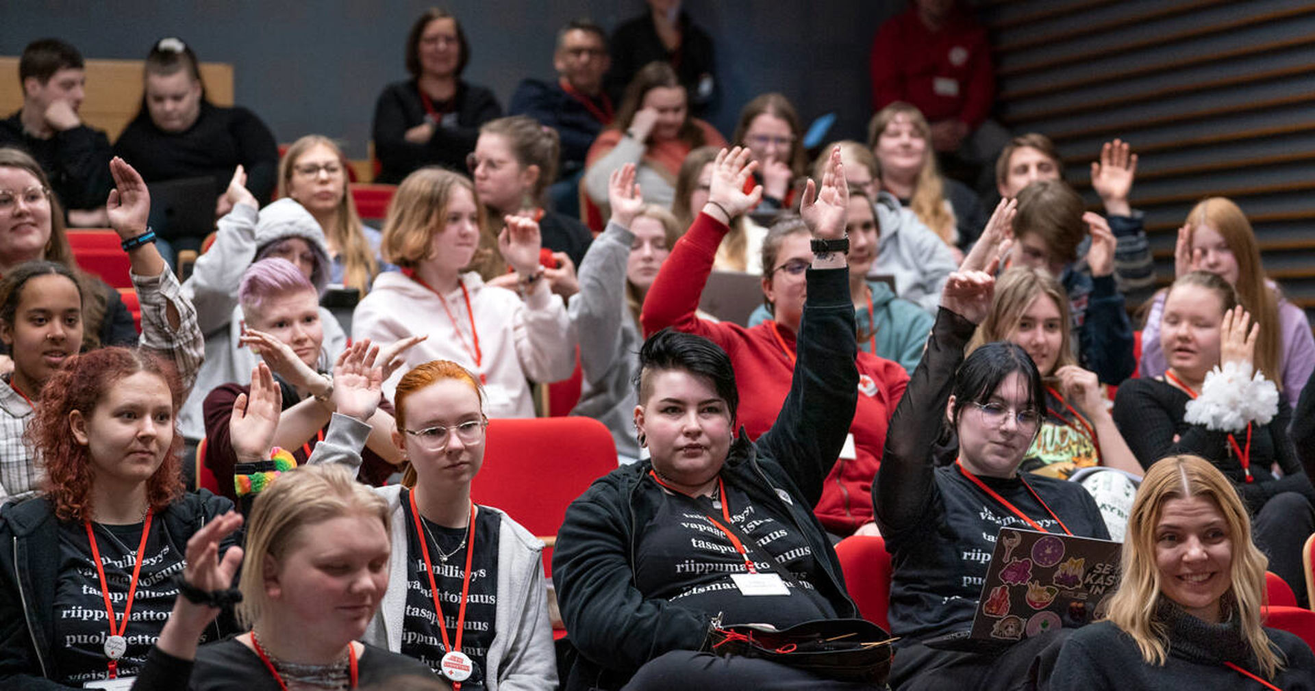 Kuvassa on useita nuoria kokouksessa. He kaikki viittaavat pyytäen puheenvuoroa.