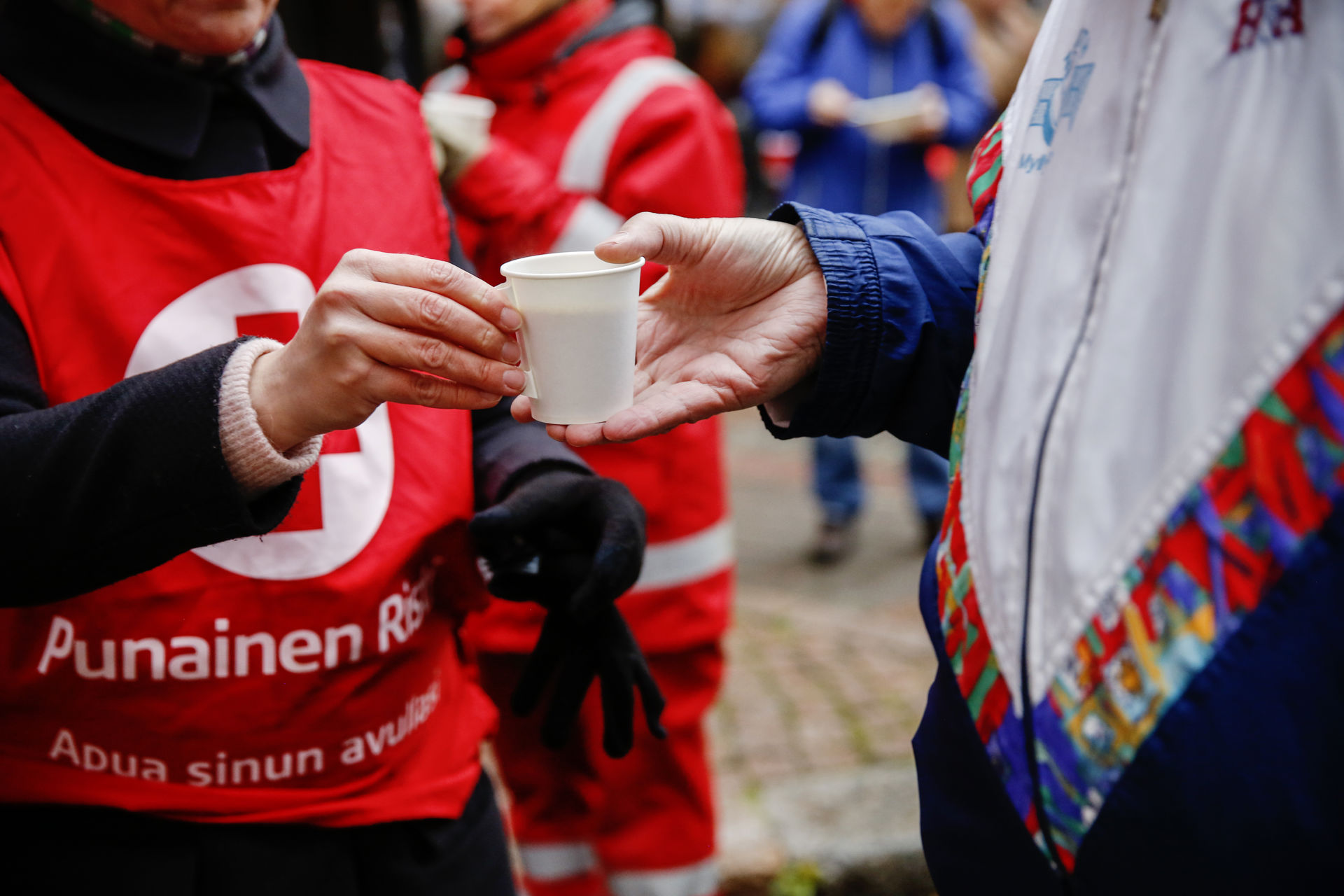 Vapaaehtoisen käsi ojentaa kahvimukia henkilölle.