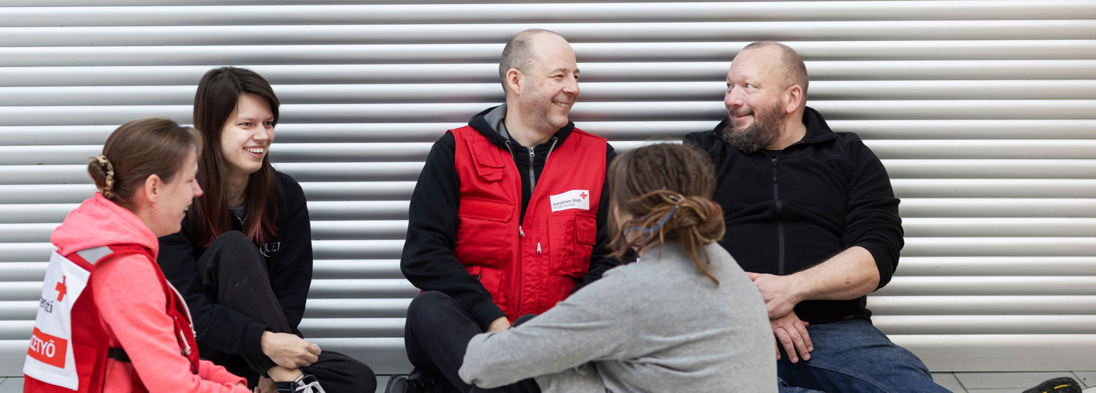 Punaisen Ristin päihdetyön vapaaehtoiset keskustelevat henkilöiden kanssa lattialla. Kaikki hymyilevät toisilleen.