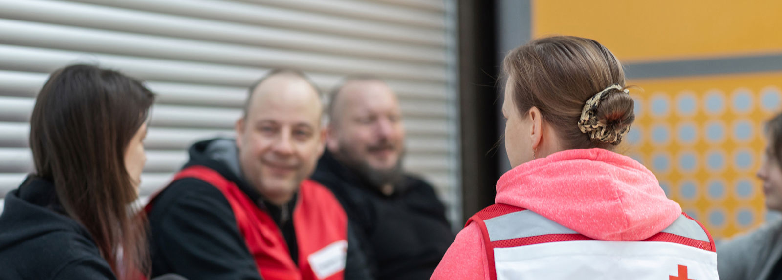 Suomen Punaisen Ristin vapaaehtoiset juttelevat porukalle ihmisiä. Yksi vapaaehtoisista on selin kameraan ja hänen vapaaehtoisliivissään lukee Päihdetyö.