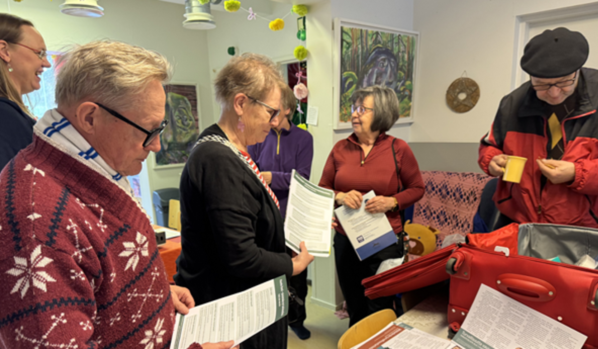 Ihmisiä esitteet käsissä ensiapulaukun ympärillä.