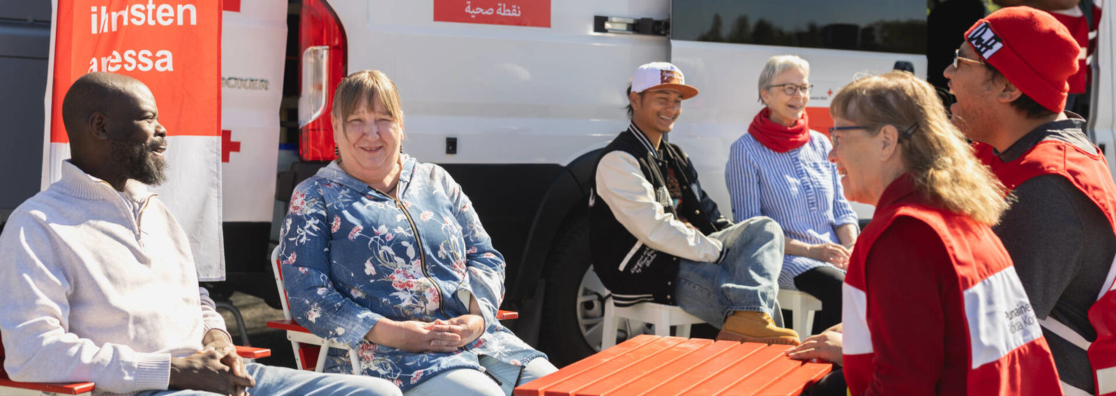 Terveyspistetoimintaryhmä keskustelee pisteellä kävijöiden kanssa liikkuvan Terveyspisteen edustalla.