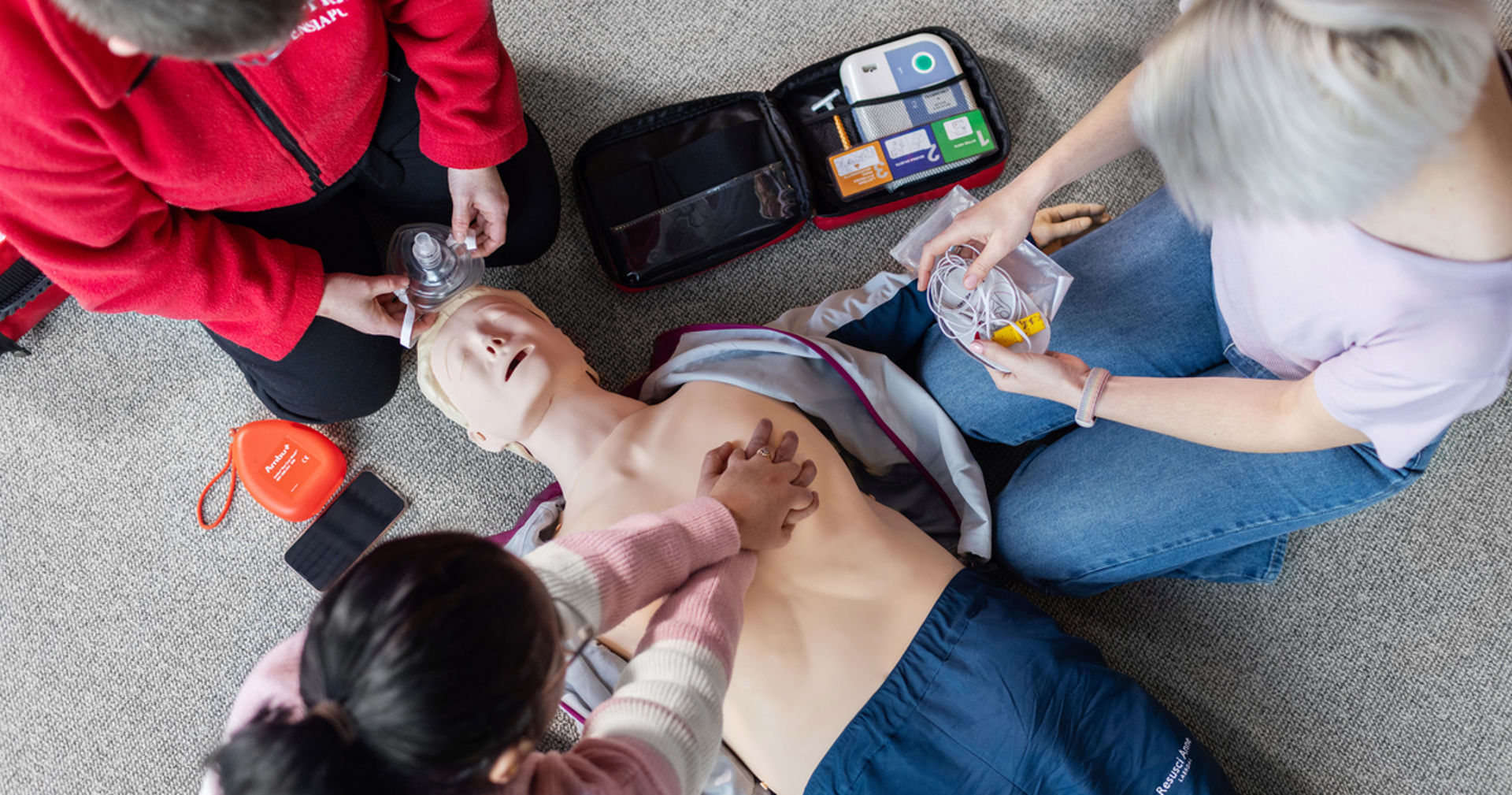 Kolme henkilöä elvytysnuken ympärillä.