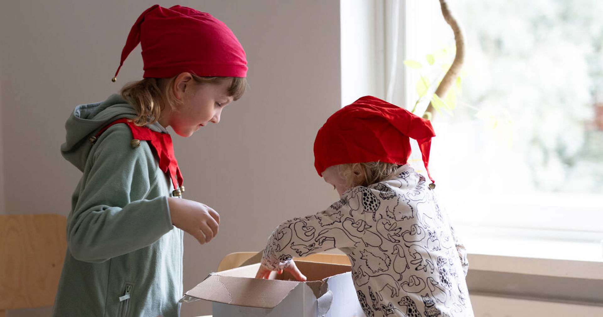 Kaksi lasta leipovat pipareita tonttulakit päässä.