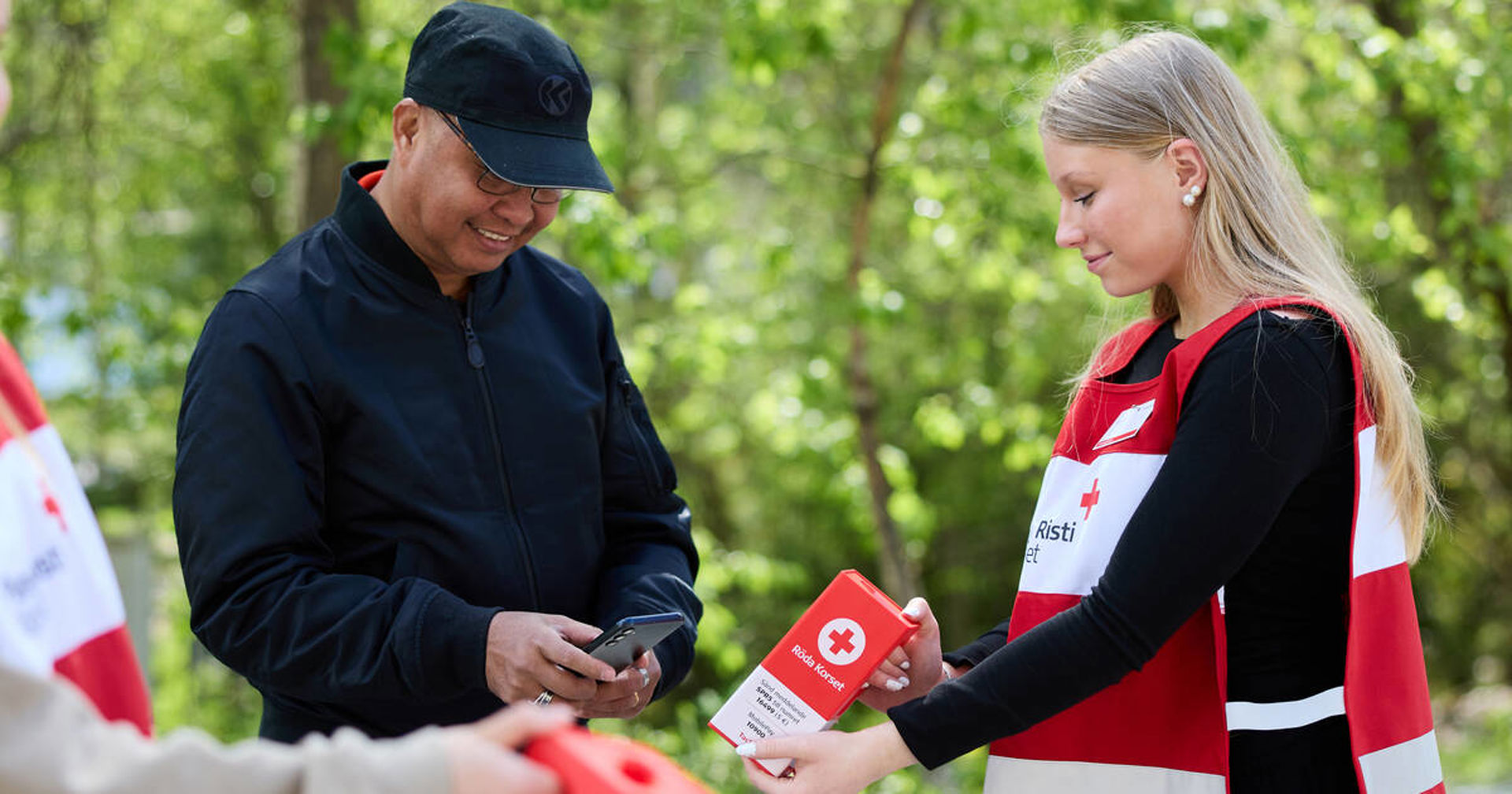 Punaisen Ristin vapaaehtoinen ojentaa keräyslipasta toiselle henkilölle.