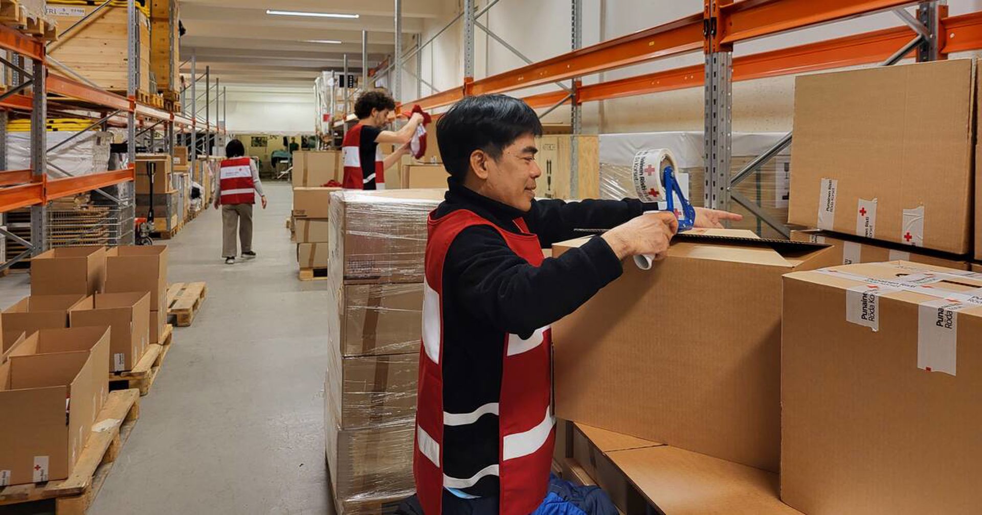 Punaisen Ristin vapaaehtoinen pakkaa laatikoita varastolla.