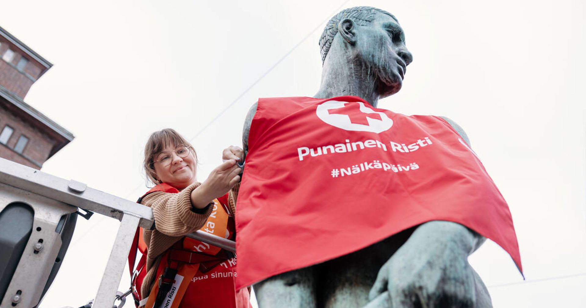 Henkilö pukee patsaalle Nälkäpäiväliiviä.