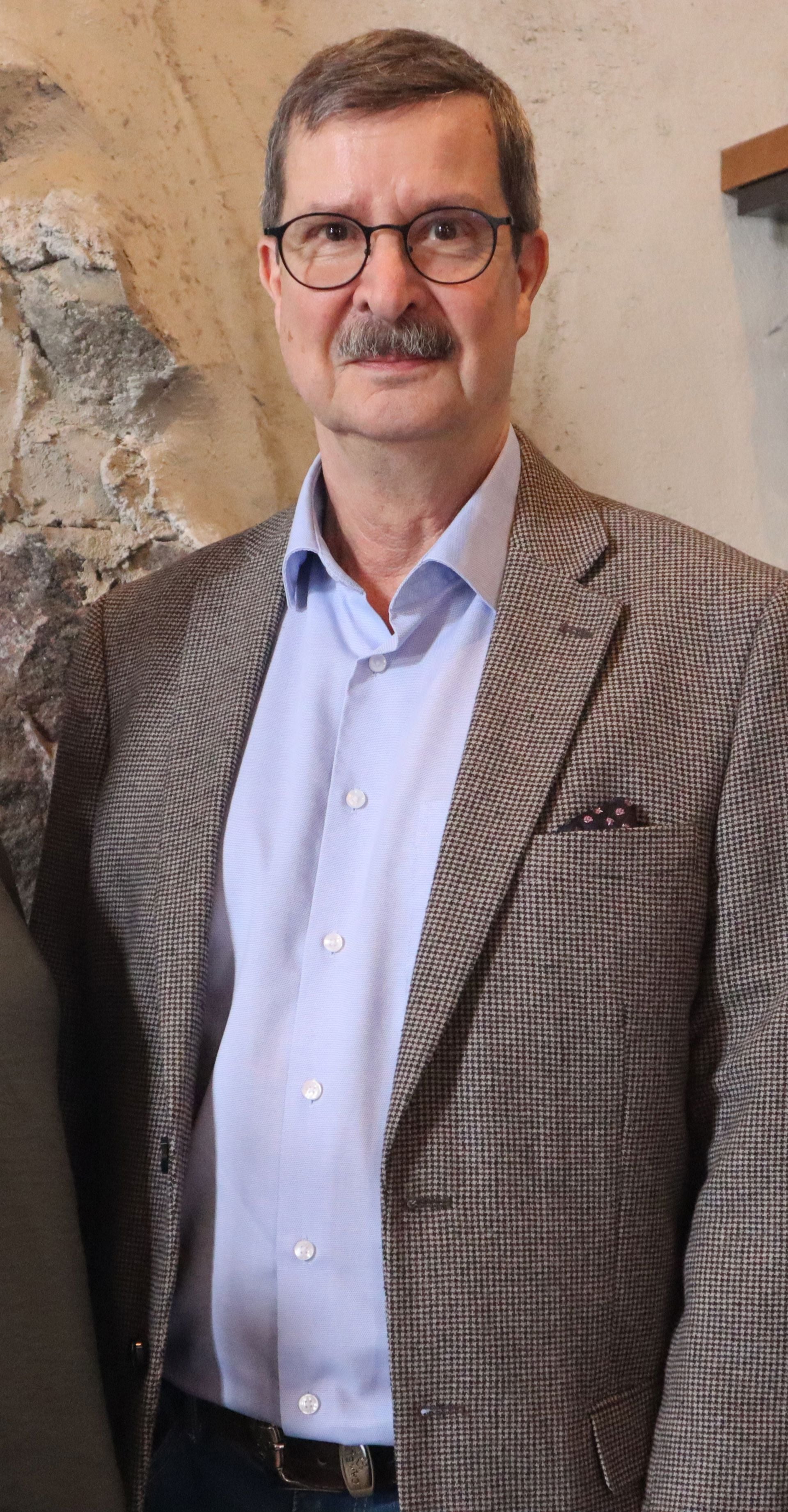 Kenneth Nygård katsoo kohti kameraa, päällään vaalea kauluspaita ja ruskeasävyinen pikkutakki.